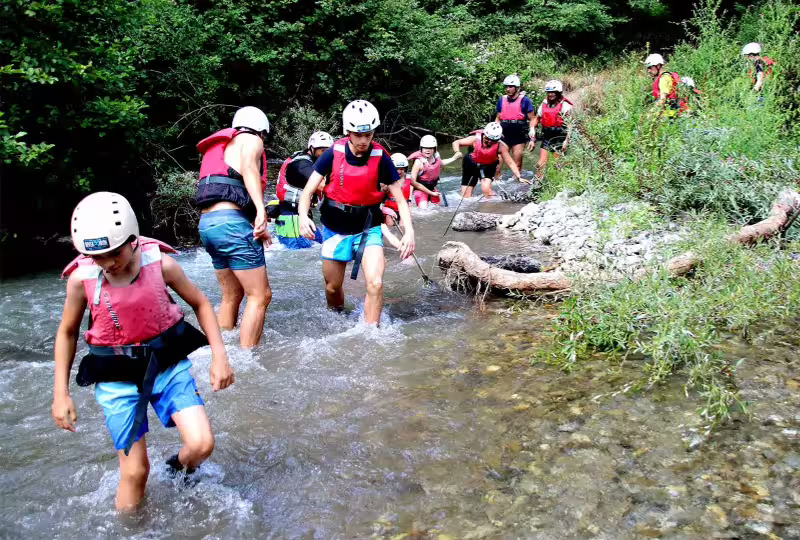 Family group canyoning in a shallow river in Pollino National Park, Calabria, enjoying summer adventure in helmets and vests