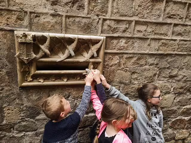 Children exploring a whimsical stone wall during a family-friendly churros and hot chocolate tour in Barcelona.