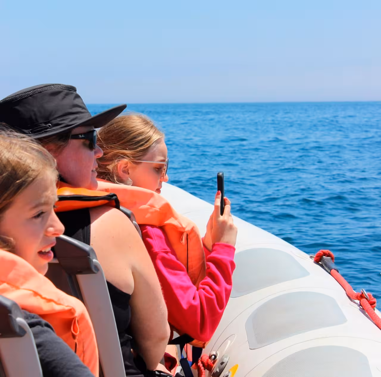 Family enjoys dolphin watching tour, capturing ocean views from a boat in life jackets.