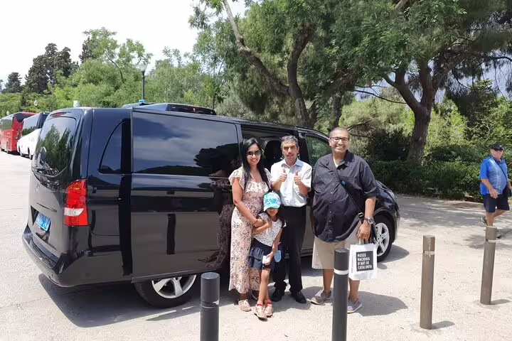 Family preparing for Girona City + Costa Brava tour beside a sleek black van under sunny skies.