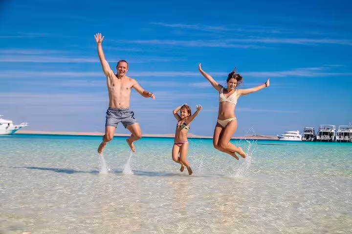 Family jumping in shallow turquoise water at White Island on a private VIP boat snorkeling tour from Sharm
