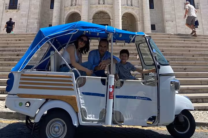 Family riding a Lisbon tuk-tuk outside Jerónimos Monastery on a 2-hour sightseeing tour and sunset cruise