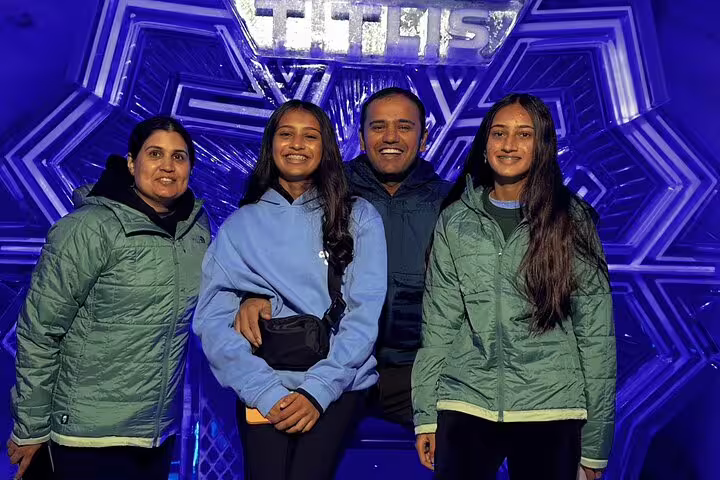 A family poses happily in front of a blue-lit ice sculpture at Mount Titlis, enjoying their Engelberg day trip.