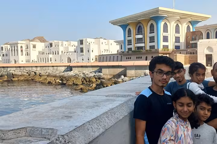 Family posing by Muttrah Corniche with Al Alam Palace and waterfront architecture in the background on a half-day Muscat city tour