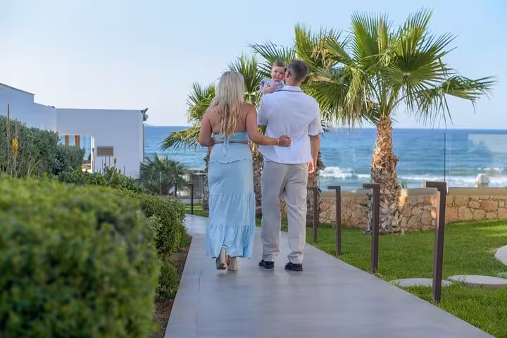 Family strolling along a scenic coastal path in Analipsi, with palm trees and ocean views, ideal for a private photoshoot.