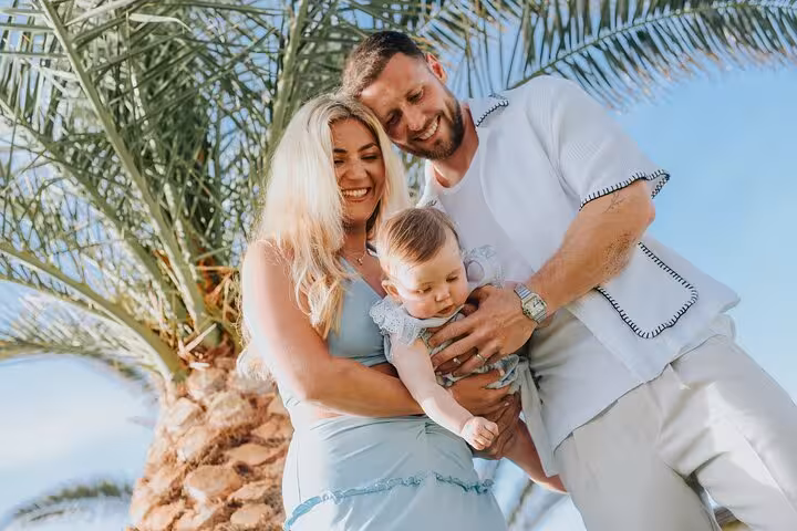 Smiling family with baby under palm trees in Analipsi captures joyful moments in a picturesque photoshoot.
