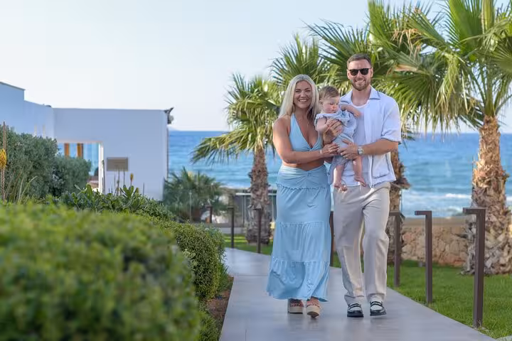 Smiling family enjoying a stroll by the sea against a backdrop of lush greenery and palm trees in Analipsi.