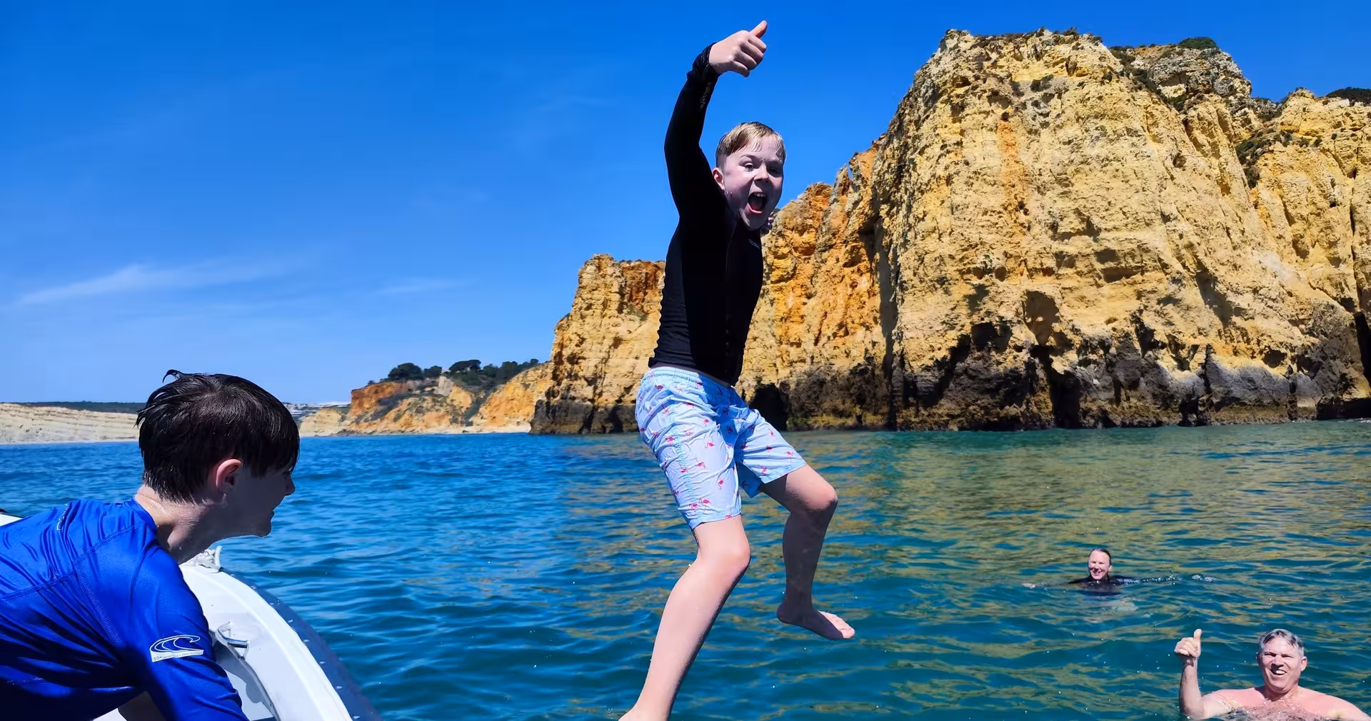 Family enjoying a Ponta da Piedade boat tour in Lagos with kids jumping into the clear Algarve sea by golden cliffs