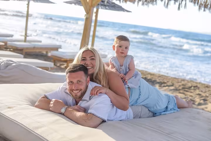 Family enjoying a private photoshoot on a beach in Analipsi, with parents and baby lounging under straw umbrellas.