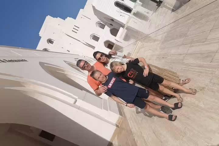 Happy family explores Muscat on a private sightseeing tour, standing by white marble architecture under clear blue skies