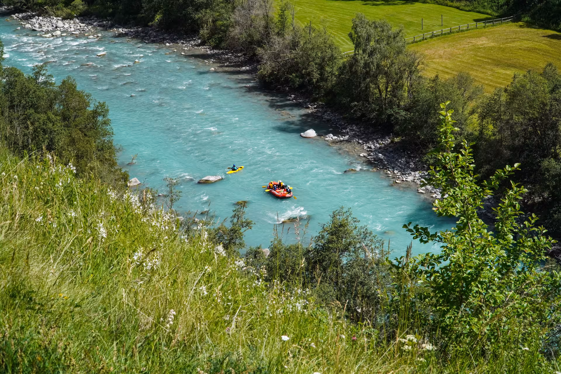 Aerial view of a family rafting adventure on the turquoise river in Engadin, with lush green landscapes and kayakers.