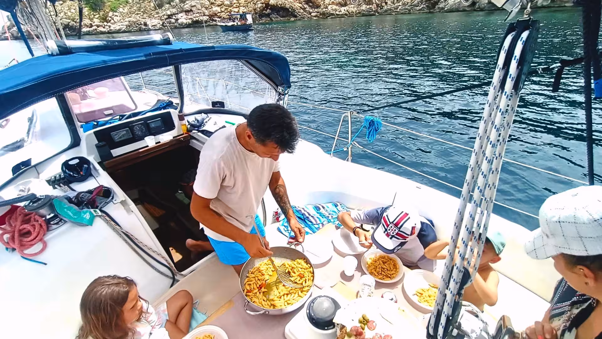 Family enjoying pasta lunch on a sailboat during Porto Conte Park tour from Alghero, Sardinia.