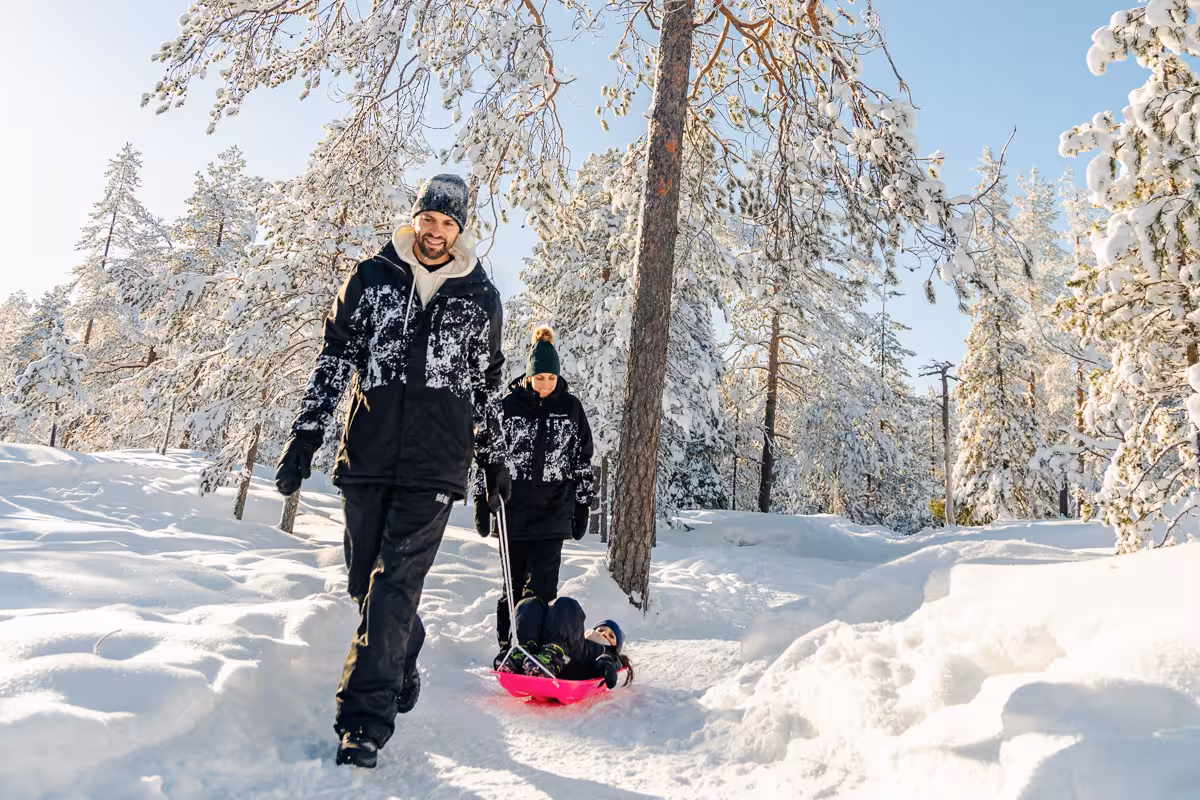 Family enjoying a sled ride in a snowy Rovaniemi forest, perfect for a holiday photo session.