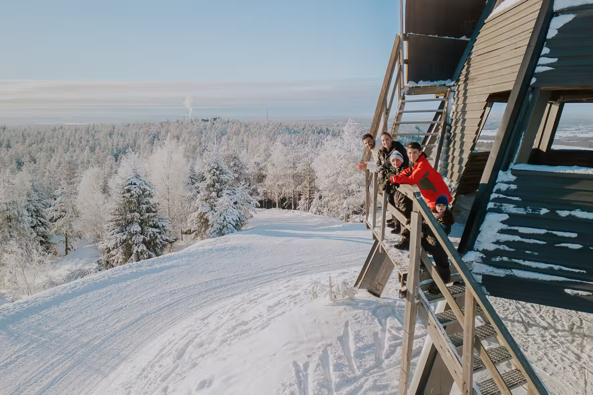 Family poses on a snowy balcony with panoramic views of Rovaniemi's winter wonderland.
