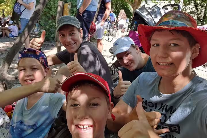 Family team gives thumbs up during Munich scavenger hunt self-guided tour in a leafy city park