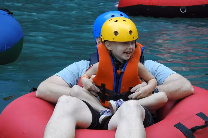 Child and adult happily tubing down Rio Celeste, enjoying a family-friendly adventure in Costa Rica's natural beauty.