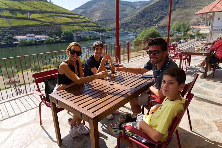 Family enjoying wine tasting with stunning views of Douro Valley's vineyards and river.