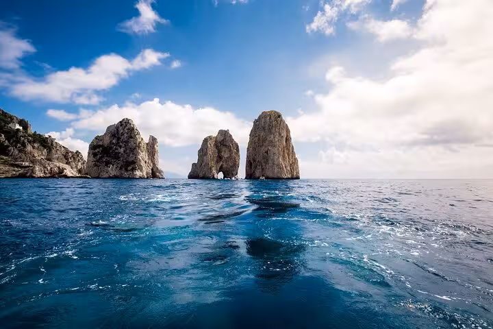 View of the iconic Faraglioni rock formations in Capri from a hydrofoil tour, under a clear blue sky.