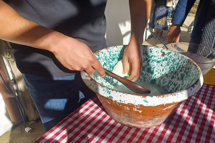 Hands stirring fresh curds in a rustic bowl during farm cheese making on pizza, wine and limoncello tour
