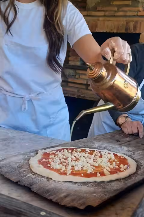 Guest drizzles olive oil on Neapolitan pizza before baking on farm tour with cheese, wine and limoncello tasting