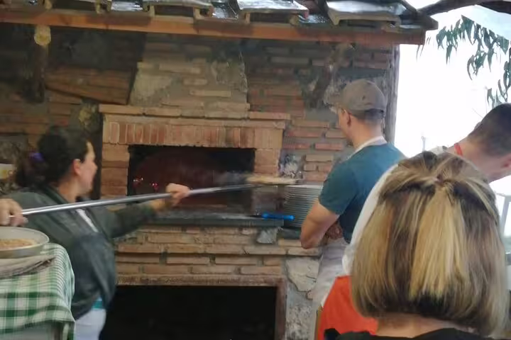 Guests baking pizza in a rustic brick oven during farm tour, with cheese tasting, wine and limoncello test