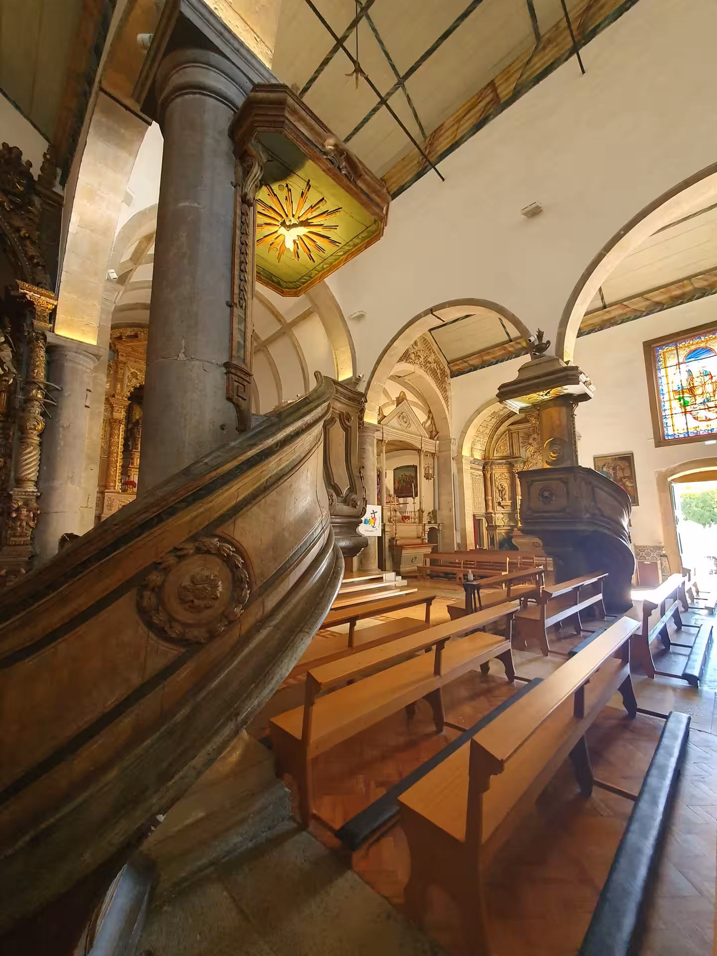 Elegant church interior in Faro with ornate wooden pulpit and rows of wooden pews under high-arched ceilings.
