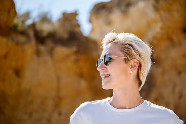 Smiling tourist enjoys sunny Faro city walk with stunning cliffs in the background.