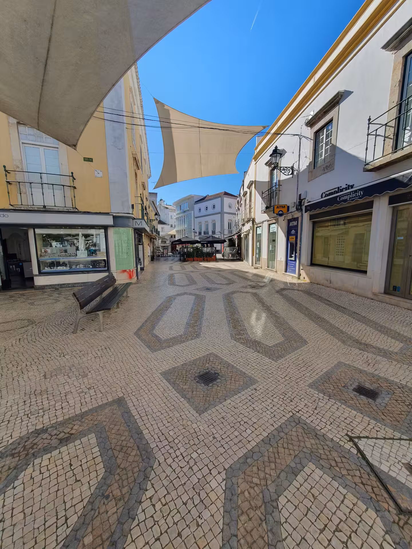 Charming Faro street with patterned cobblestones and sunshades, highlighting Algarve's architectural beauty.