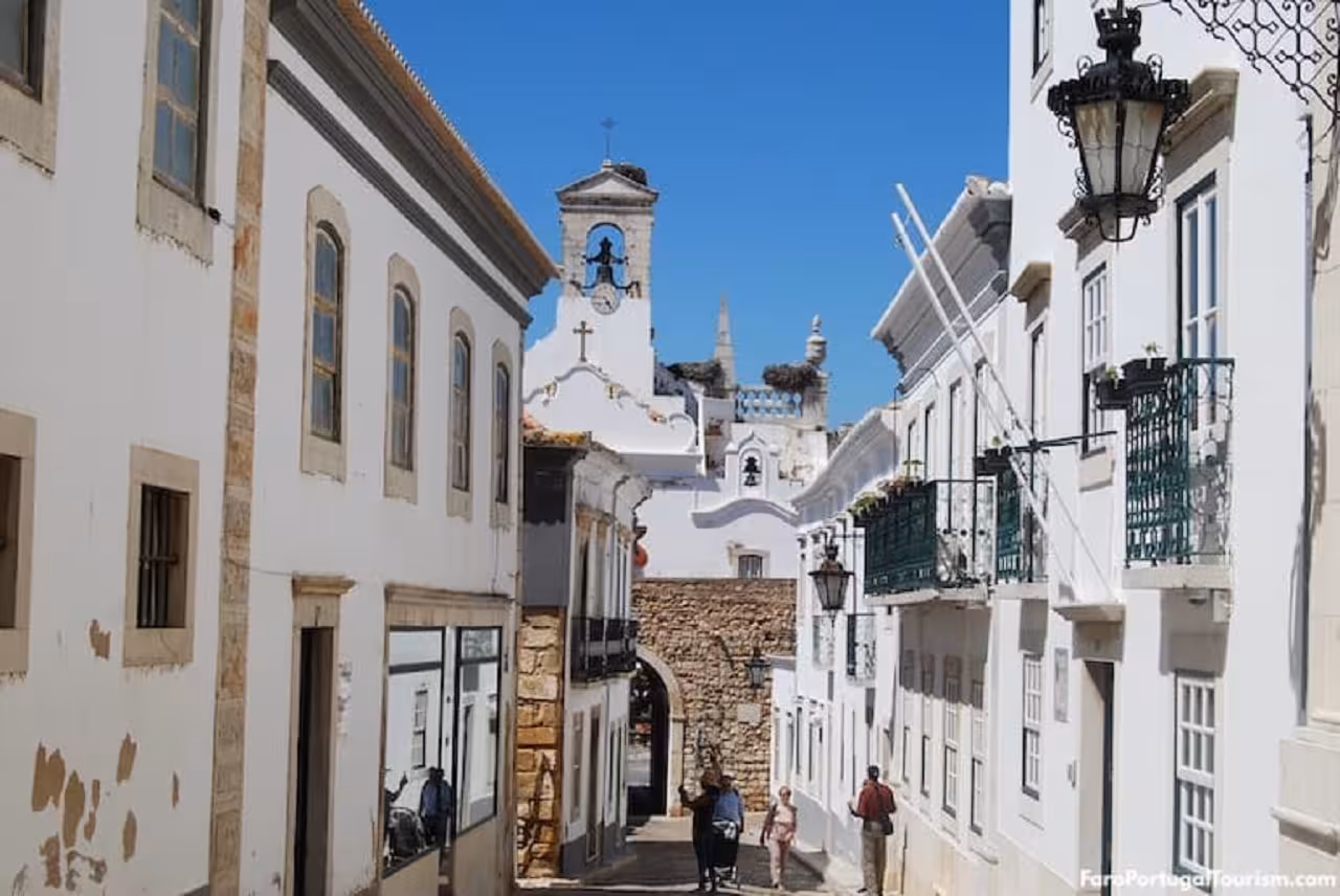 Narrow cobbled lane in Faro historic center with whitewashed houses, church tower and city walls on an Eastern Algarve tour