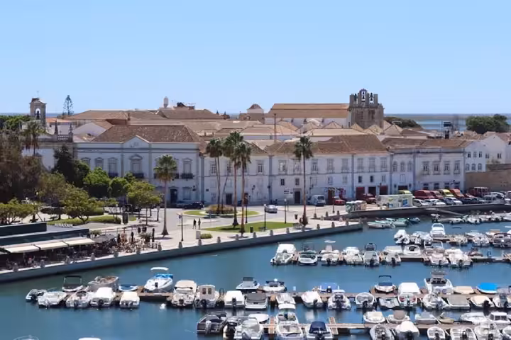 Boats moored in Faro marina with historic whitewashed buildings and palm-lined promenade on an Eastern Algarve full-day tour