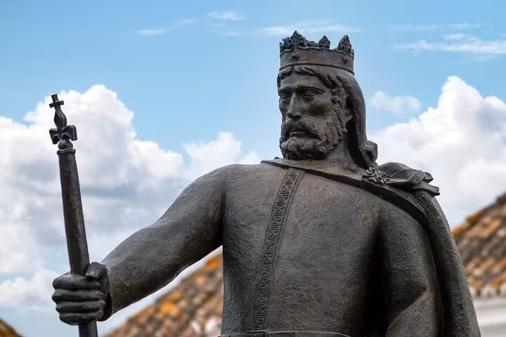 Majestic statue of a medieval king under a vibrant blue sky, a highlight of Faro's historical landmarks on the city walk.