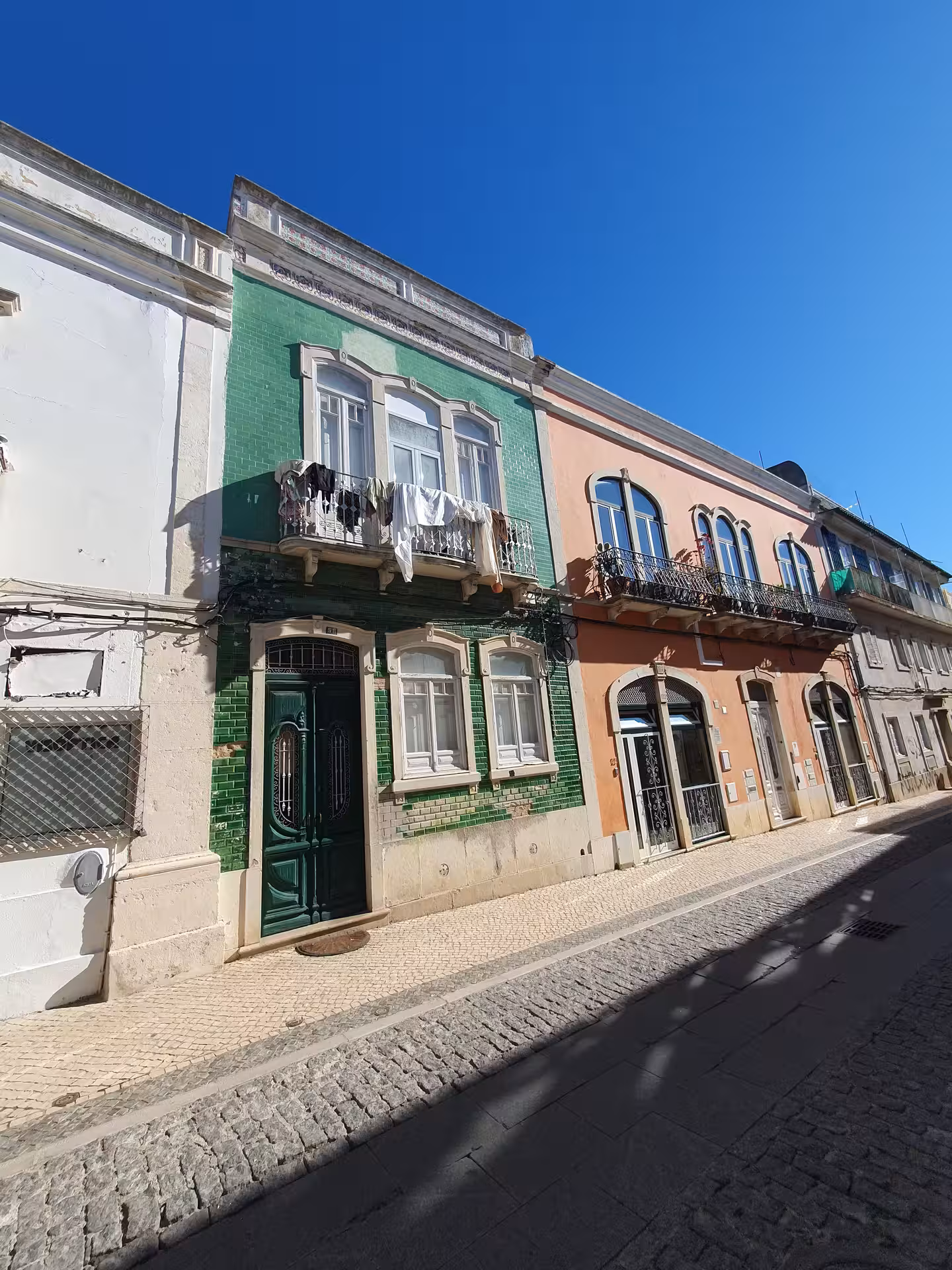 Charming Faro street with colorful facades, including a green-tiled building under a bright blue sky, perfect for walking tours.