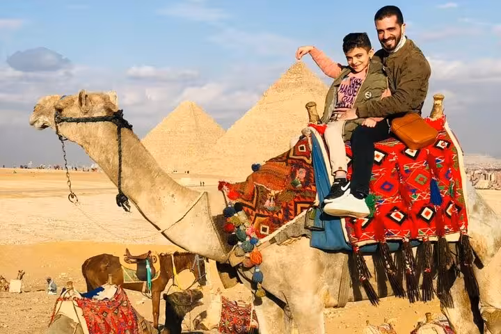 Father and child camel ride at Giza Pyramids on a private tour, enjoying Sahara desert panoramic views near Cairo