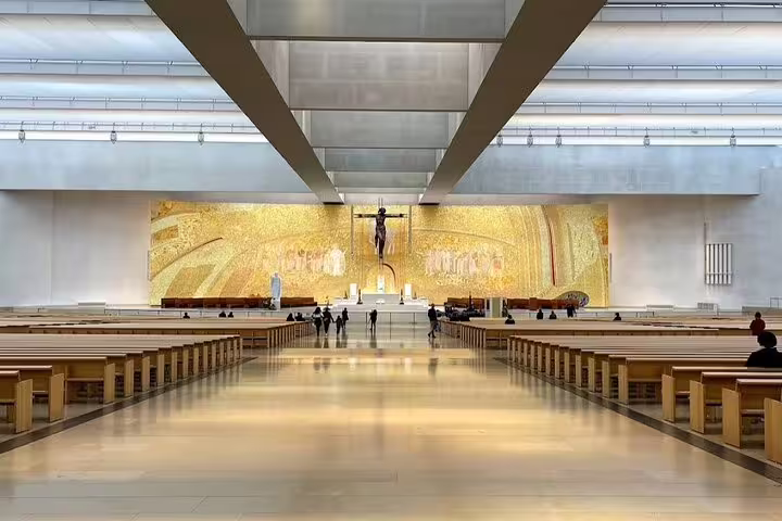Interior of the Basilica of the Holy Trinity in Fatima, featuring a spacious hall and a golden altar with religious art.