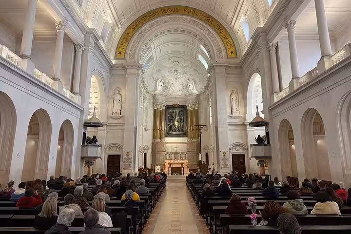 Interior of the Basilica of Our Lady of the Rosary in Fatima, filled with visitors attending a service under its grand arches.