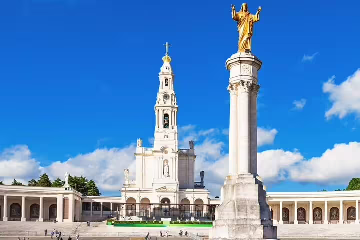 Majestic Fatima Basilica and golden statue under a clear blue sky, iconic pilgrimage site in Portugal.