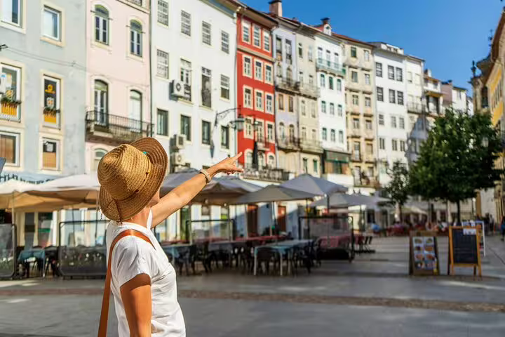 A tourist in a sun hat points at colorful historic buildings in a sunny Coimbra square during a private Fatima and Coimbra day trip from Lisbon.