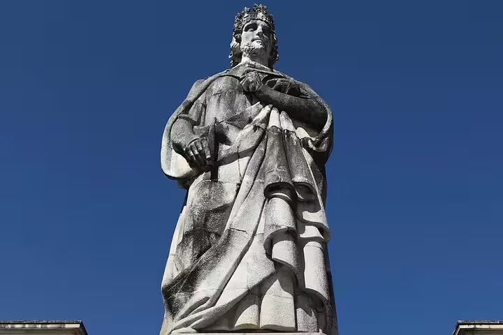 Statue of a historical figure against a clear blue sky in Coimbra, Portugal, featured in the Fatima and Coimbra Private Tour.