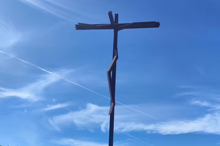 Silhouette of a modern cross sculpture against a bright blue sky at Fátima, highlighting the site's spiritual ambiance.