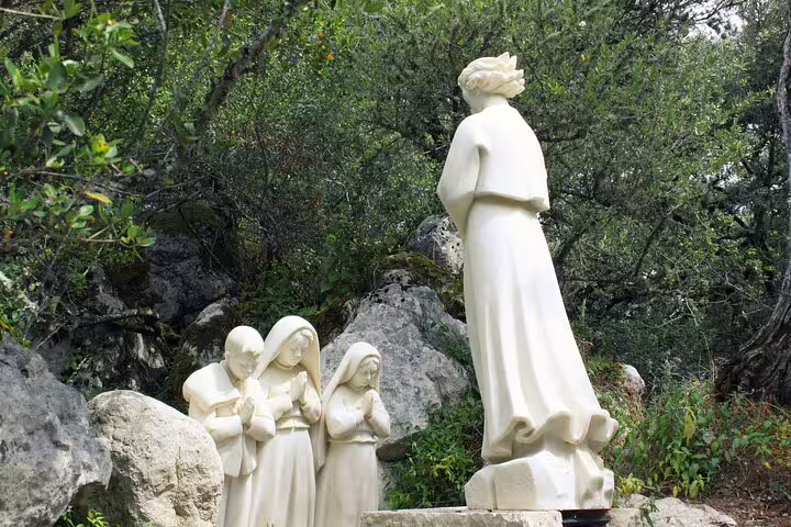 Statues depicting the Marian apparition at Fatima, surrounded by lush greenery, featured in the Lisbon to Fatima tour.