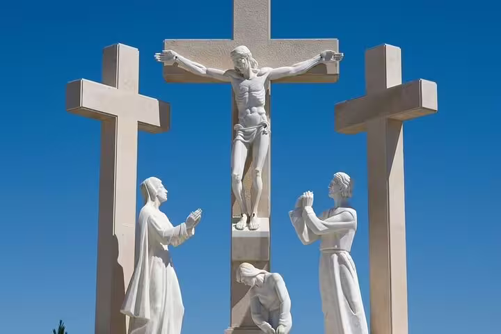 Three white stone crosses with religious sculptures under a clear blue sky at Fátima, Portugal on a small group day trip from Lisbon.
