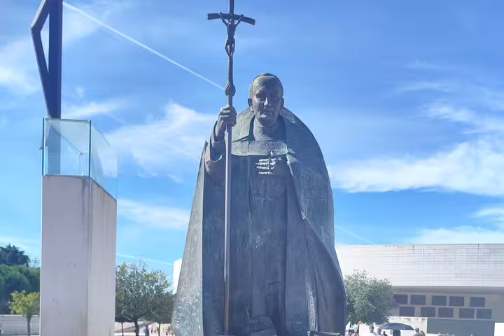 Statue of a religious figure holding a cross at Fátima, symbolizing faith and spirituality in the tranquil sanctuary.