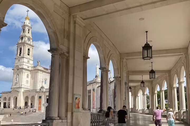 Visitors explore the arched colonnades of Fátima Sanctuary with the iconic basilica in the background.