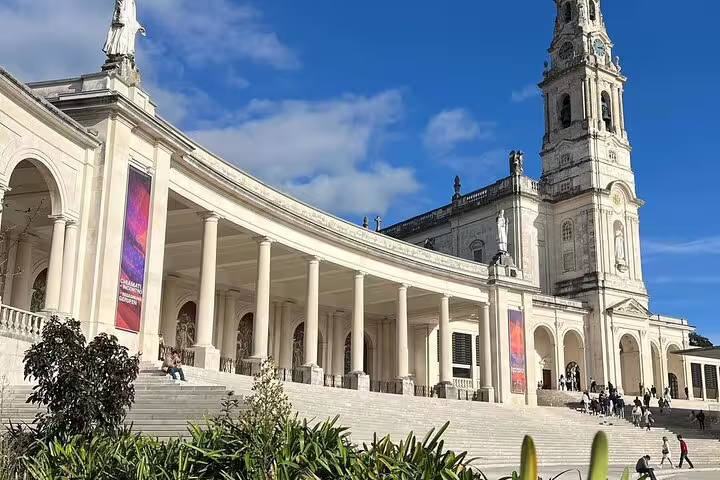 Majestic view of the Sanctuary of Fátima with its grand colonnades and basilica under a clear blue sky, ideal for a cultural tour.