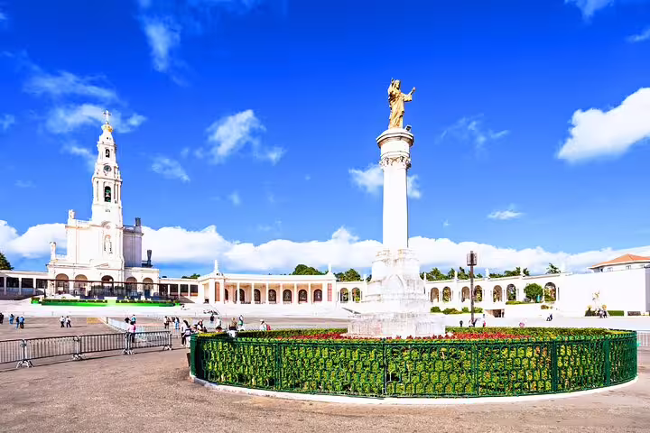 Vibrant view of Fátima Sanctuary's basilica and statue on a sunny day, featured in the Lisbon small group tour to Fátima, Nazaré, and Óbidos.