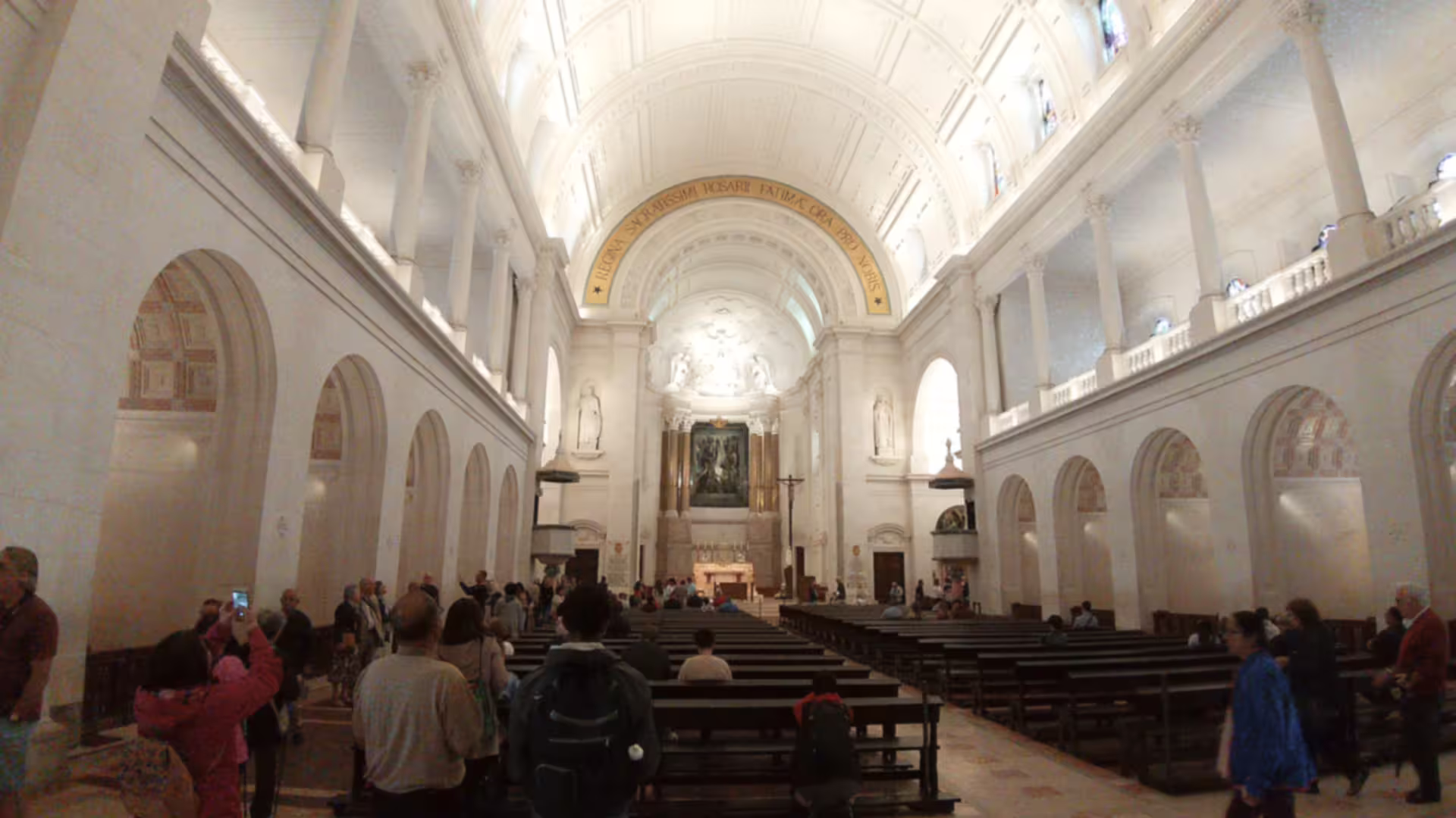 Interior view of Fátima Sanctuary with visitors exploring the sacred site, highlighting its grandeur and spiritual significance.