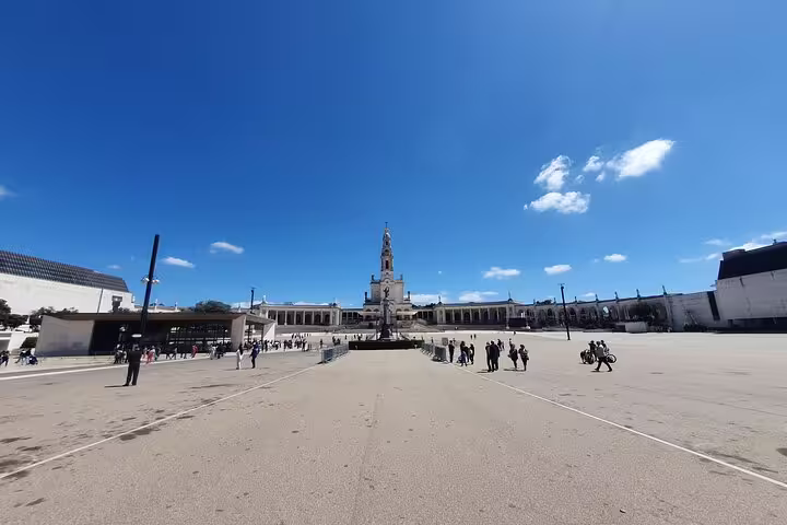 Wide-angle view of Fátima Sanctuary under clear blue skies, showcasing its grand architecture on a small-group tour from Lisbon.