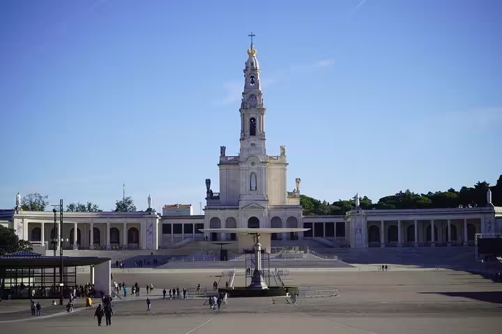Sanctuary of Our Lady of Fátima with visitors exploring the grand plaza on a sunny day during a Lisbon to Fátima private tour.