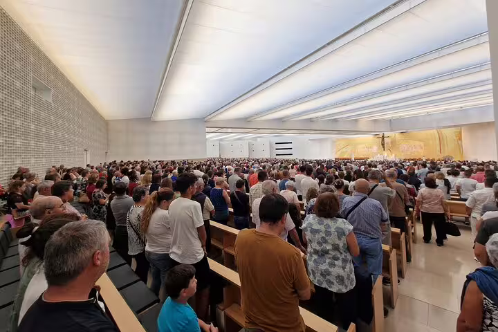 A large crowd gathers inside the modern Sanctuary of Fátima during a full-day private tour from Lisbon, highlighting Portugal's rich spiritual heritage.