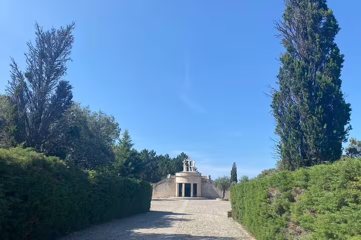Scenic pathway leading to the serene entrance of the Fátima Sanctuary, flanked by lush greenery and towering trees.